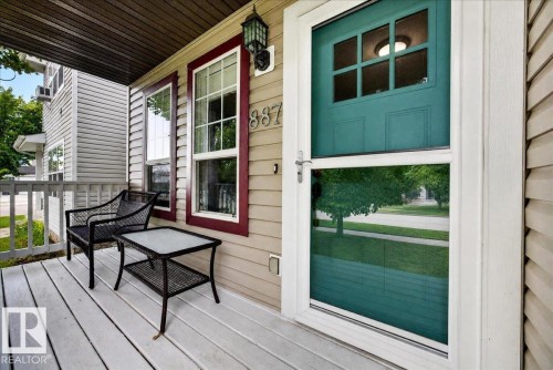 Welcoming front porch featuring a composite deck with clean lines, black metal outdoor seating, and direct access via a teal-painted entry door with multi-pane glazing - 887 Oakland Boulevard, Devon, AB - Outdoor With Deck Patio Veranda With Exterior