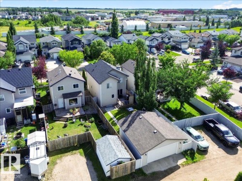 Aerial view showcasing a contemporary home with a dark-finished roof, expansive manicured lawn, mature landscaping with established trees, and detached garage - 887 Oakland Boulevard, Devon, AB - Outdoor
