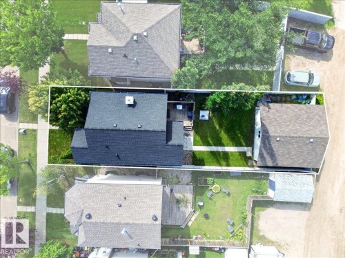 Property featuring a dark shingle roof, a paved walkway, a manicured lawn, and mature trees - 887 Oakland Boulevard, Devon, AB - 