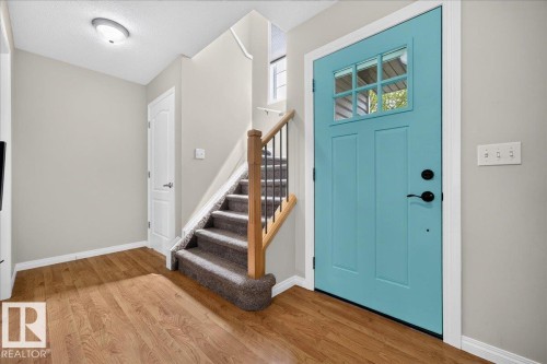 Welcoming foyer showcasing warm wood-finish flooring, a striking turquoise entry door with multi-pane glazing, and a staircase with wood railings and metal balusters - 887 Oakland Boulevard, Devon, AB - Indoor Photo Showing Other Room