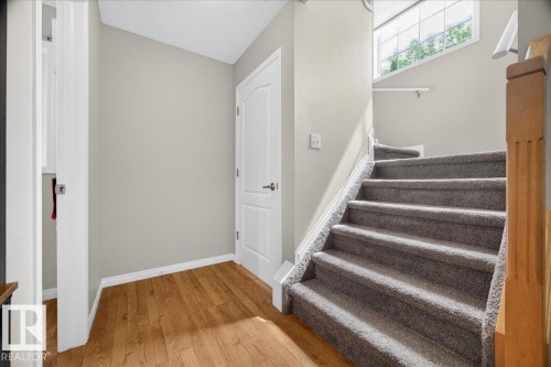 Welcoming foyer with warm wood-finish flooring, white panel doors, neutral wall finishes, and a staircase featuring carpeted treads with white painted railings - 887 Oakland Boulevard, Devon, AB - Indoor Photo Showing Other Room