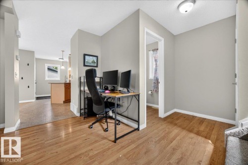 Versatile home office featuring wood-finish flooring throughout, dedicated workspace with dual-monitor setup, abundant natural lighting from recessed ceiling fixtures, and direct access to adjoining rooms - 887 Oakland Boulevard, Devon, AB - Indoor Photo Showing Office