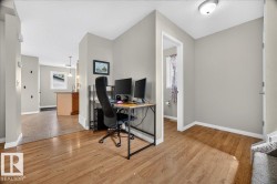 Versatile home office featuring wood-finish flooring throughout, dedicated workspace with dual-monitor setup, abundant natural lighting from recessed ceiling fixtures, and direct access to adjoining rooms - 