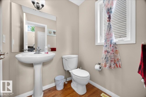 Pedestal sink with chrome faucet, large mirror, and wood-finish flooring - 887 Oakland Boulevard, Devon, AB - Indoor Photo Showing Bathroom