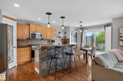 Open-concept kitchen and dining area featuring warm wood-finish flooring, recessed lighting, and a stone-clad kitchen island with pendant lighting - 