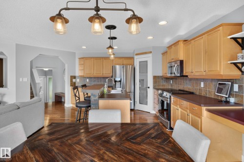 Open-concept kitchen and dining area featuring warm-toned wood cabinetry, stainless steel appliances, a center island with bar seating, and hard-surface countertops - 21 Nash Close, St. Albert, AB - Indoor Photo Showing Kitchen
