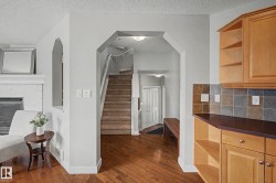 Hardwood-style flooring extends through an arched entryway leading to a carpeted staircase - 