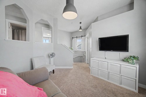 Carpeted living area featuring a wall-mounted television, recessed shelving, and suspended pendant lighting - 21 Nash Close, St. Albert, AB - Indoor Photo Showing Other Room