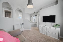 Carpeted living area featuring a wall-mounted television, recessed shelving, and suspended pendant lighting - 