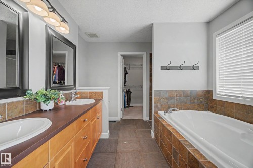 Spacious bathroom featuring a dual vanity, built-in soaking tub with tiled surround, and ceramic tile flooring - 21 Nash Close, St. Albert, AB - Indoor Photo Showing Bathroom