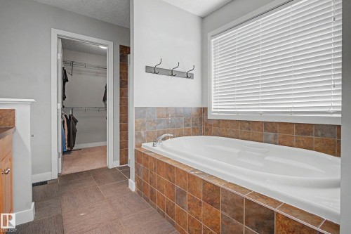 Soaking tub with a tiled surround, complemented by a window with blinds and dark tile flooring - 21 Nash Close, St. Albert, AB - Indoor Photo Showing Bathroom