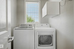 Dedicated laundry area featuring a window with blinds, a wall-mounted storage cabinet, and a white paneled door with a silver handle - 