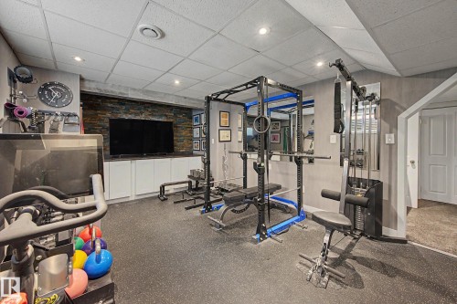 Dedicated fitness area featuring rubber flooring, recessed lighting, a stone accent wall, built-in cabinetry, and a mirrored wall - 21 Nash Close, St. Albert, AB - Indoor Photo Showing Gym Room