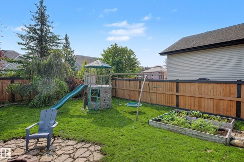 Expansive backyard featuring a manicured lawn, established trees, a raised garden bed, and a wooden privacy fence - 21 Nash Close, St. Albert, AB - Outdoor With Backyard