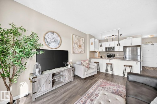 Open-concept living space with wood-finish flooring, a kitchen island with seating, stainless steel appliances, white cabinetry, and recessed lighting - #238 1008 Rosenthal Bv Nw, Edmonton, AB - Indoor