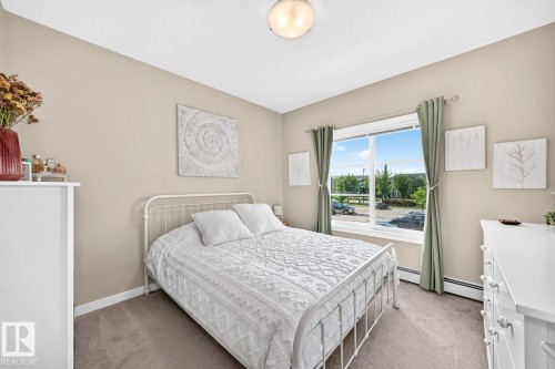 Bright secondary bedroom featuring a metal bed frame, carpeted flooring, and large windows with natural light - #238 1008 Rosenthal Bv Nw, Edmonton, AB - Indoor Photo Showing Bedroom
