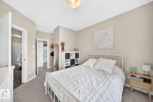 Bright primary bedroom featuring a metal bed frame, soft neutral wall tones, and carpeted flooring - #238 1008 Rosenthal Bv Nw, Edmonton, AB - Indoor Photo Showing Bedroom