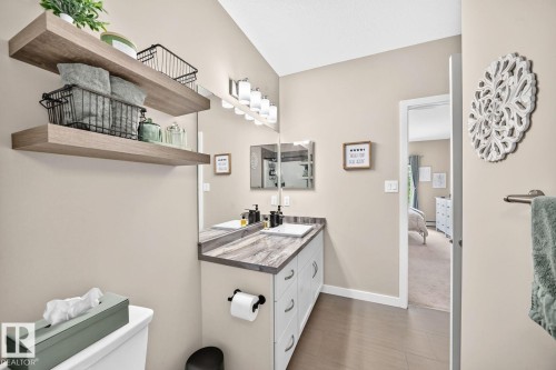 Dual floating shelves, double vanity with integrated sinks, contemporary light fixture, large wall mirror, and wood-finish flooring - #238 1008 Rosenthal Bv Nw, Edmonton, AB - Indoor Photo Showing Bathroom