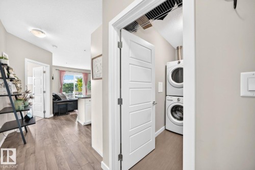 Wood-finish flooring, recessed lighting, and a laundry closet with stacked appliances - #238 1008 Rosenthal Bv Nw, Edmonton, AB - Indoor Photo Showing Laundry Room