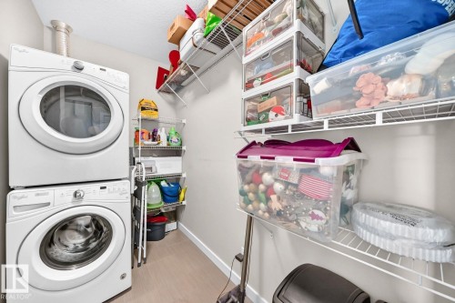 Dedicated laundry room featuring stacked front-load washers and dryers with white finishes, wire shelving with organized storage containers, and neutral flooring throughout - #238 1008 Rosenthal Bv Nw, Edmonton, AB - Indoor Photo Showing Laundry Room