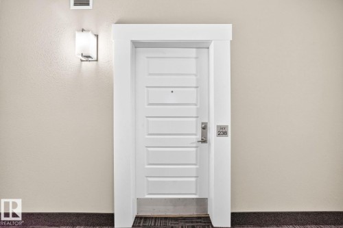 Six-panel door with substantial white trim, featuring a satin nickel lever handle and wall-mounted sconce - #238 1008 Rosenthal Bv Nw, Edmonton, AB -  Photo Showing Other Room