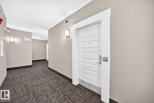Neutral wall color, wall-mounted light fixtures, white door with horizontal paneling, dark textured flooring, and white trim - #238 1008 Rosenthal Bv Nw, Edmonton, AB - Indoor Photo Showing Other Room