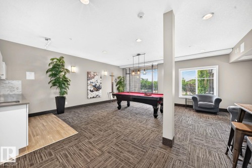 Spacious common area featuring patterned carpet flooring, a large window, a built-in countertop with backsplash, and recessed lighting - #238 1008 Rosenthal Bv Nw, Edmonton, AB - Indoor