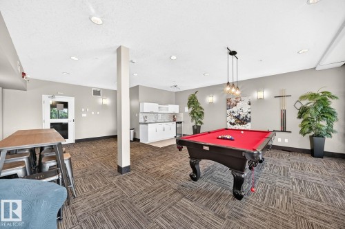 Expansive recreational space featuring patterned carpet flooring, a built-in wet bar with white cabinetry and a tiled backsplash, recessed lighting, and a prominent billiard table with pendant lighting overhead - #238 1008 Rosenthal Bv Nw, Edmonton, AB - Indoor Photo Showing Other Room