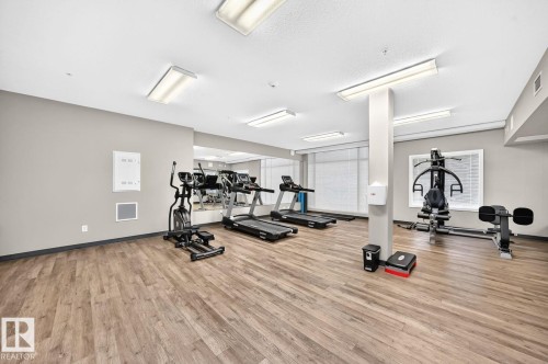 Fitness room featuring wood-finish flooring, fluorescent lighting, and mirrored walls - #238 1008 Rosenthal Bv Nw, Edmonton, AB - Indoor Photo Showing Gym Room