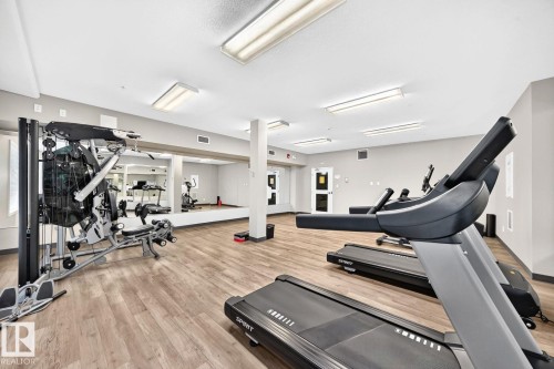 State-of-the-art fitness facility featuring wood-finish flooring, recessed and linear ceiling lighting, and a comprehensive array of cardio and strength training equipment - #238 1008 Rosenthal Bv Nw, Edmonton, AB - Indoor Photo Showing Gym Room
