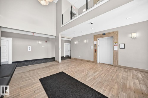 Wood-finish tile flooring throughout, high ceilings with recessed lighting, and a modern chandelier - #238 1008 Rosenthal Bv Nw, Edmonton, AB - Indoor Photo Showing Other Room