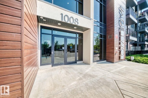 Modern building entrance featuring wood-finish siding, full-light entry doors, and large windows - #238 1008 Rosenthal Bv Nw, Edmonton, AB - Outdoor