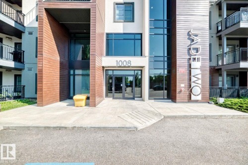 Modern building exterior featuring a wood-finish facade, expansive glass windows, and a paved entry - #238 1008 Rosenthal Bv Nw, Edmonton, AB - Outdoor With Balcony