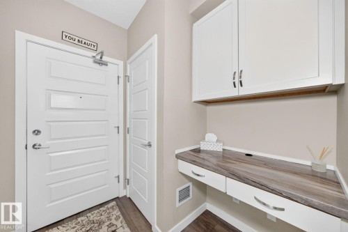 Entryway featuring a built-in desk with a wood-finish countertop, white upper and lower cabinetry, and wood-finish flooring - #238 1008 Rosenthal Bv Nw, Edmonton, AB - Indoor Photo Showing Other Room