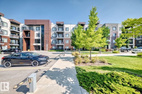 Modern multi-story building featuring a prominent entrance, private balconies, and an adjacent parking area - #238 1008 Rosenthal Bv Nw, Edmonton, AB - Outdoor With Balcony With Facade