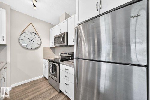 Modern kitchen featuring stainless steel refrigerator with freezer drawer, white cabinetry with brushed nickel hardware, black electric range with oven, and wood-finish flooring throughout - #238 1008 Rosenthal Bv Nw, Edmonton, AB - Indoor Photo Showing Kitchen With Upgraded Kitchen
