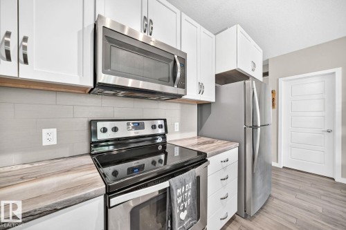 Updated kitchen featuring white cabinetry with chrome hardware, stainless steel appliances including a double electric range and over-the-range microwave, wood-finish countertops, subway tile backsplash, and stainless steel refrigerator - #238 1008 Rosenthal Bv Nw, Edmonton, AB - Indoor Photo Showing Kitchen