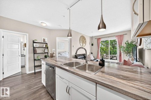 Kitchen island with an undermount double-basin sink, gooseneck faucet, and integrated dishwasher - #238 1008 Rosenthal Bv Nw, Edmonton, AB - Indoor Photo Showing Kitchen With Double Sink