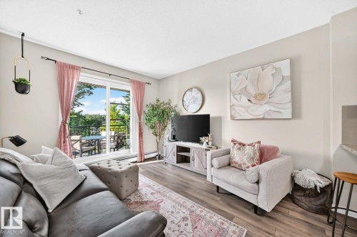 Sliding glass doors to outdoor balcony, wood-finish flooring, recessed lighting, media console, and built-in breakfast bar - #238 1008 Rosenthal Bv Nw, Edmonton, AB - Indoor Photo Showing Living Room