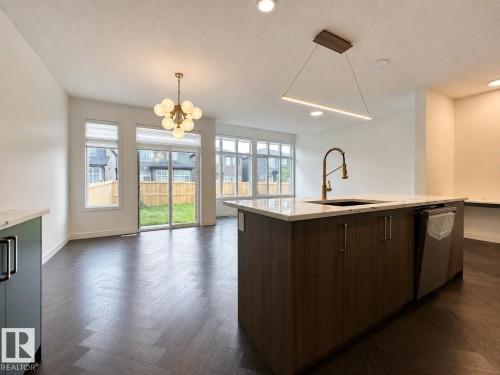 Kitchen island featuring a single-basin sink with a brass faucet, integrated dishwasher, and a light-toned countertop - 5478 Kootook Road Sw, Edmonton, AB - Indoor Photo Showing Kitchen
