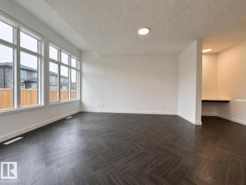 Spacious room featuring dark wood-finish flooring in a herringbone pattern, extensive multi-pane windows, crisp white walls, and a recessed built-in desk area with overhead lighting - 5478 Kootook Road Sw, Edmonton, AB - Indoor Photo Showing Other Room