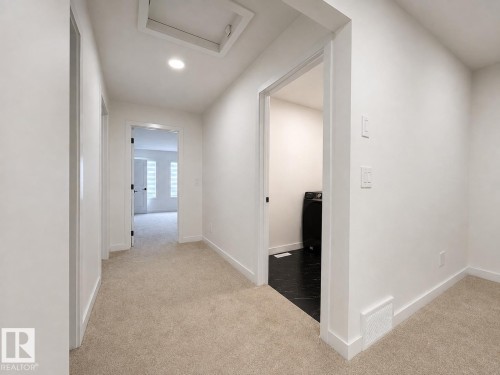 Carpeted hallway with white walls and trim, leading to a room with dark flooring and a black appliance - 5478 Kootook Road Sw, Edmonton, AB - Indoor Photo Showing Other Room