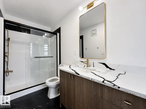 Modern bathroom featuring a wood-finish vanity with a white and black veined countertop, a gold-framed rectangular mirror, and a walk-in shower with a black-framed glass enclosure - 5478 Kootook Road Sw, Edmonton, AB - Indoor Photo Showing Bathroom