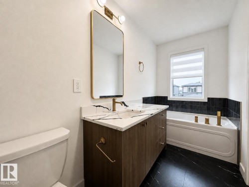Bathroom featuring a wood-finish vanity with a white countertop, gold-tone hardware, and a rectangular mirror - 5478 Kootook Road Sw, Edmonton, AB - Indoor Photo Showing Bathroom