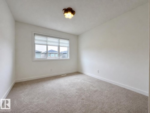 Bright room featuring a window with integrated blinds, neutral-toned carpet flooring, white baseboards, and a decorative ceiling light fixture - 5478 Kootook Road Sw, Edmonton, AB - Indoor Photo Showing Other Room