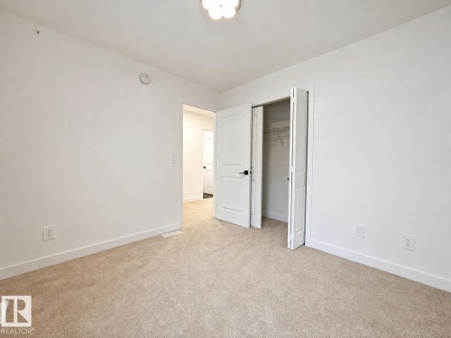 Carpeted room with white walls, a white bi-fold closet door, and a white interior door with black hardware - 5478 Kootook Road Sw, Edmonton, AB - Indoor Photo Showing Other Room