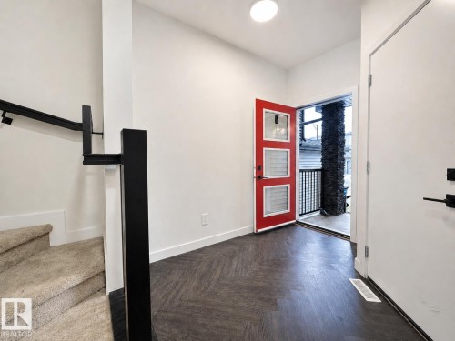 Entryway featuring a striking red door with frosted glass panels, dark wood-finish flooring, and a contemporary black metal stair railing - 5478 Kootook Road Sw, Edmonton, AB - Indoor Photo Showing Other Room