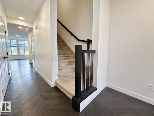 Interior hallway and staircase featuring dark wood-finish herringbone flooring, white walls, and recessed lighting - 5478 Kootook Road Sw, Edmonton, AB - Indoor Photo Showing Other Room