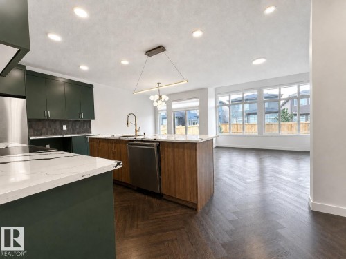 Contemporary kitchen featuring dark green cabinetry, a central island with wood-finish paneling, and white countertops with dark veining - 5478 Kootook Road Sw, Edmonton, AB - Indoor Photo Showing Kitchen With Upgraded Kitchen