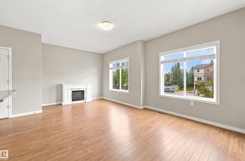 Spacious living area featuring wood-finish flooring, a white electric fireplace, and two large windows with blinds - #144 104 West Haven Dr, Leduc, AB - Indoor Photo Showing Other Room